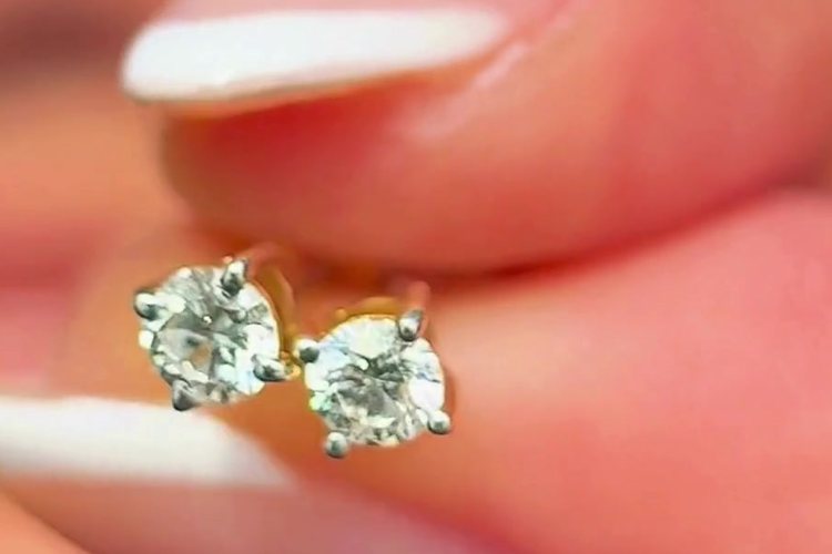 Two lab-grown diamond studs held between fingertips